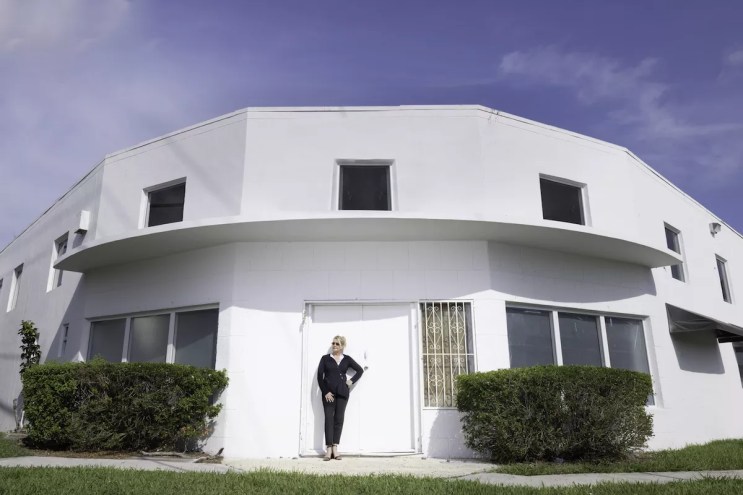 photo of woman standing in the doorway of a two-story white building on a corner lot