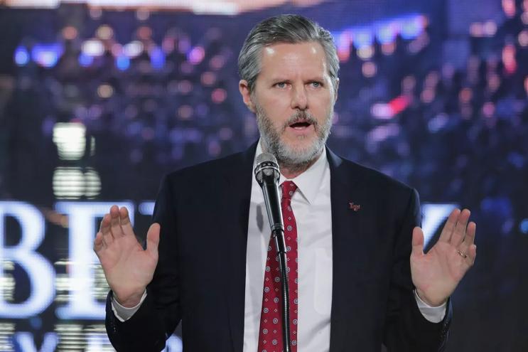 Photo of a bearded Jerry Falwell Jr. standing at a podium, with both hands raised, palms facing out