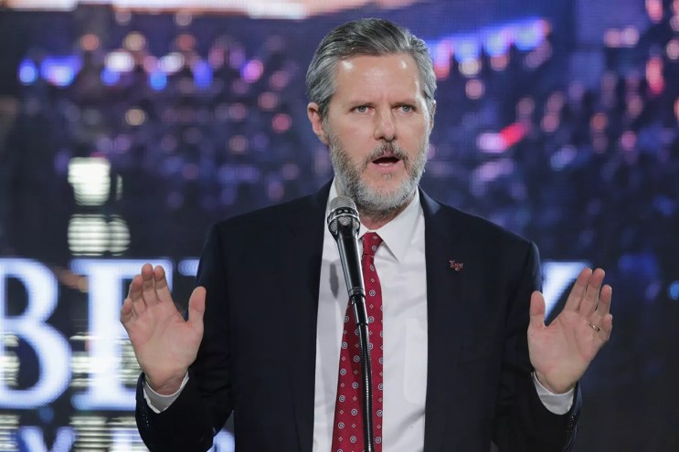Photo of a bearded Jerry Falwell Jr. standing at a podium, with both hands raised, palms facing out