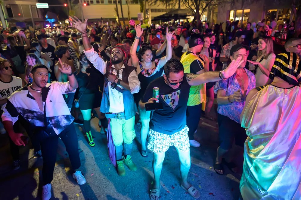 a group of revelers in costume dancing under colored lights on Lincoln Road in Miami Beach