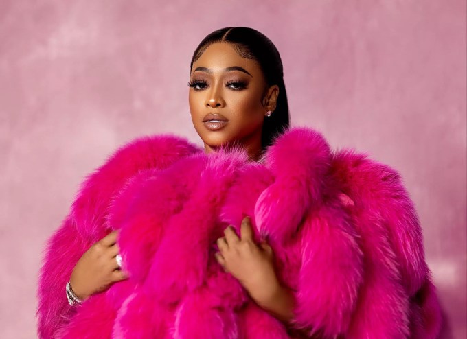 Rapper Trina wearing a pink fur coat while standing against a soft-pink background