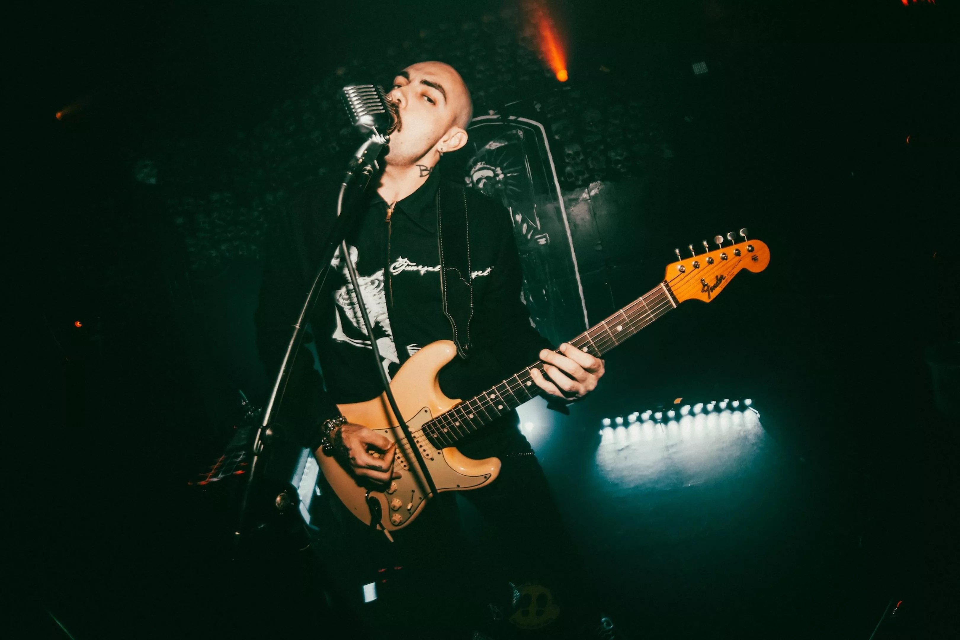 Miami musician Niko Javan singing into a microphone and strumming his guitar, performing as Blood Orchid