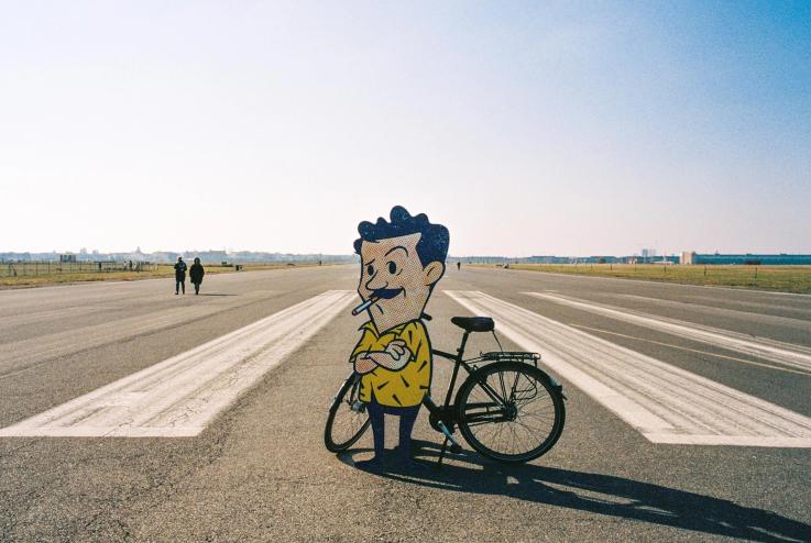 Gene On Earth's animated character in front of a bike while standing on a runway.