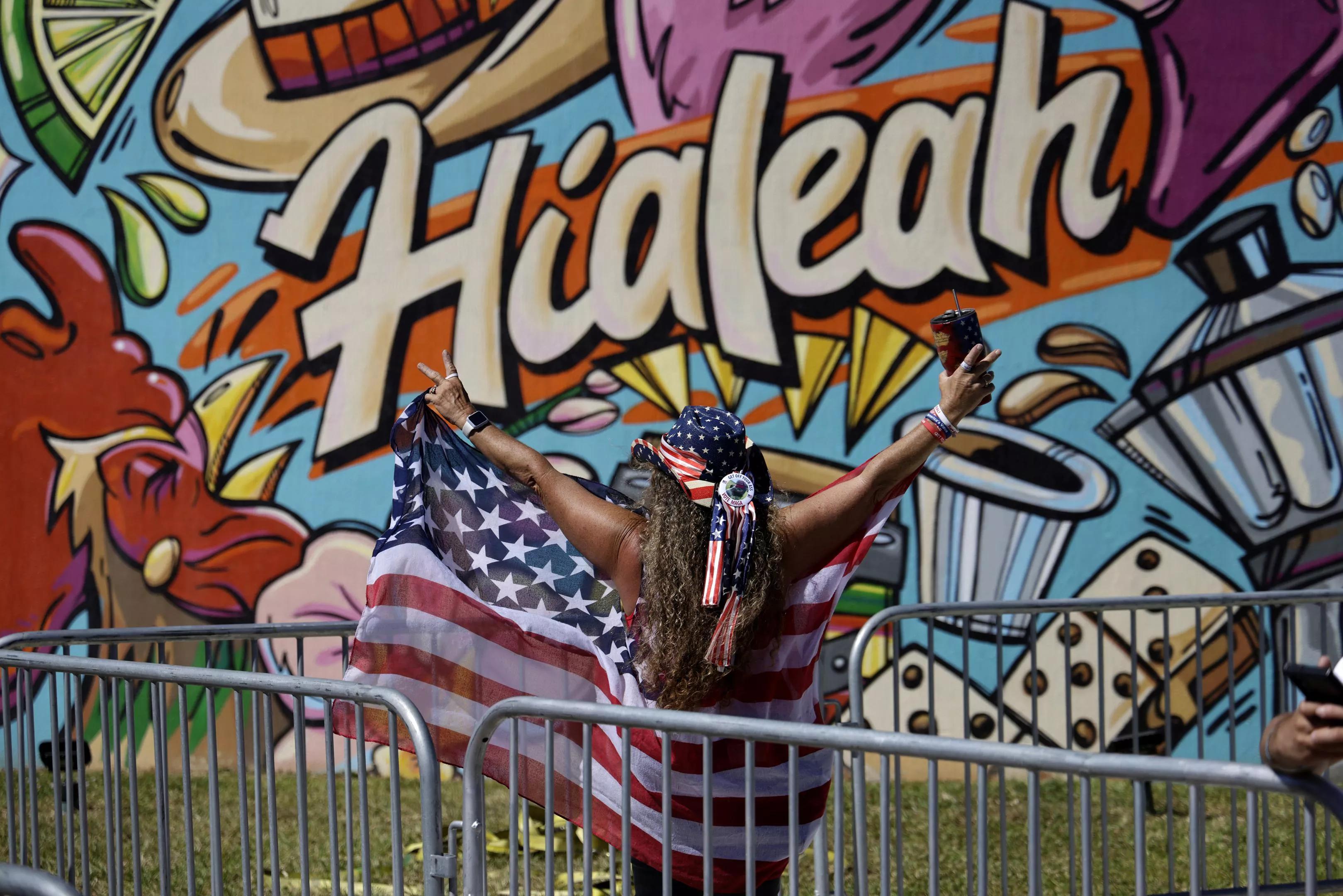 A woman draped in an American flag stands in front of graffiti