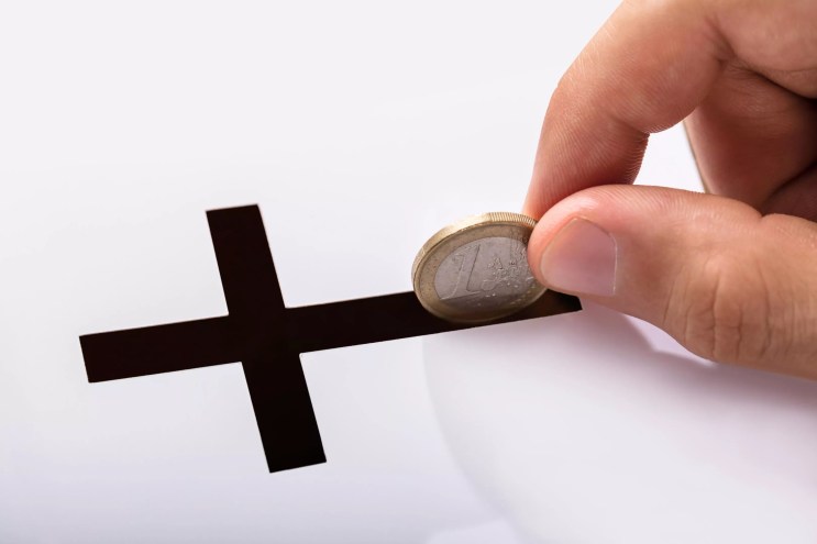 A coin being dropped into a crucifix slot.