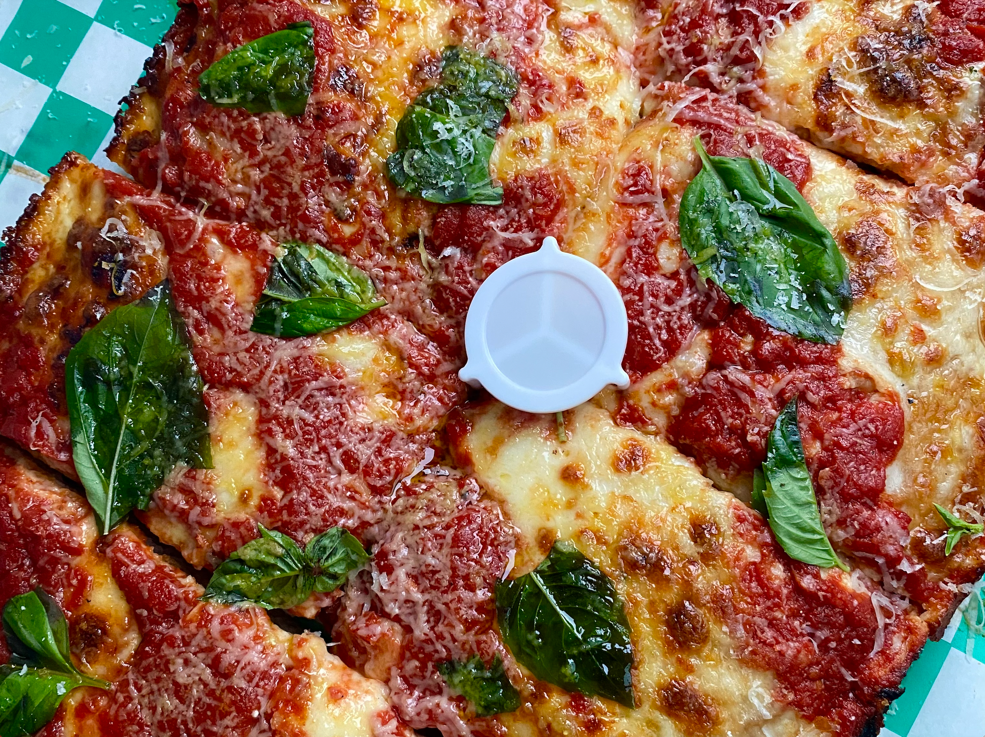 A close-up photo of a pizza from Old Greg's Pizza covered in cheese and basil
