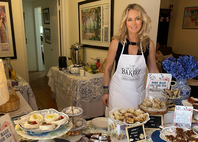 A blonde woman poses next to pastries on a table