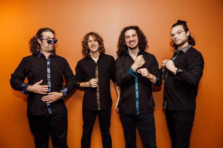 The four members of Pigeons Playing Ping Pong against a bright orange wall