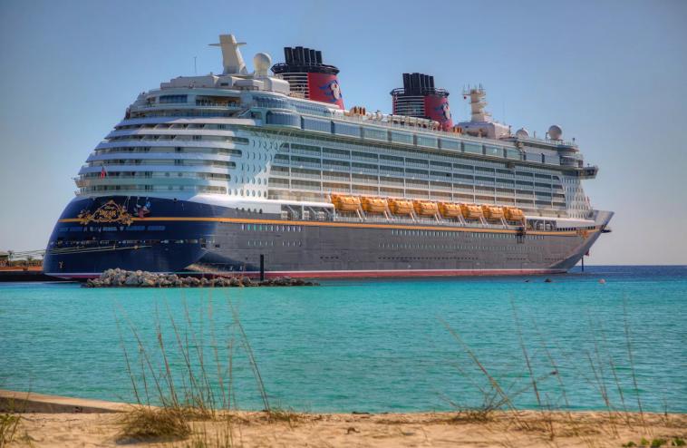 The Disney Dream cruise ship –– a massive vessel colored navy, white, and red –– arrives to shore in turquoise blue waters Castaway Cay, Bahamas.
