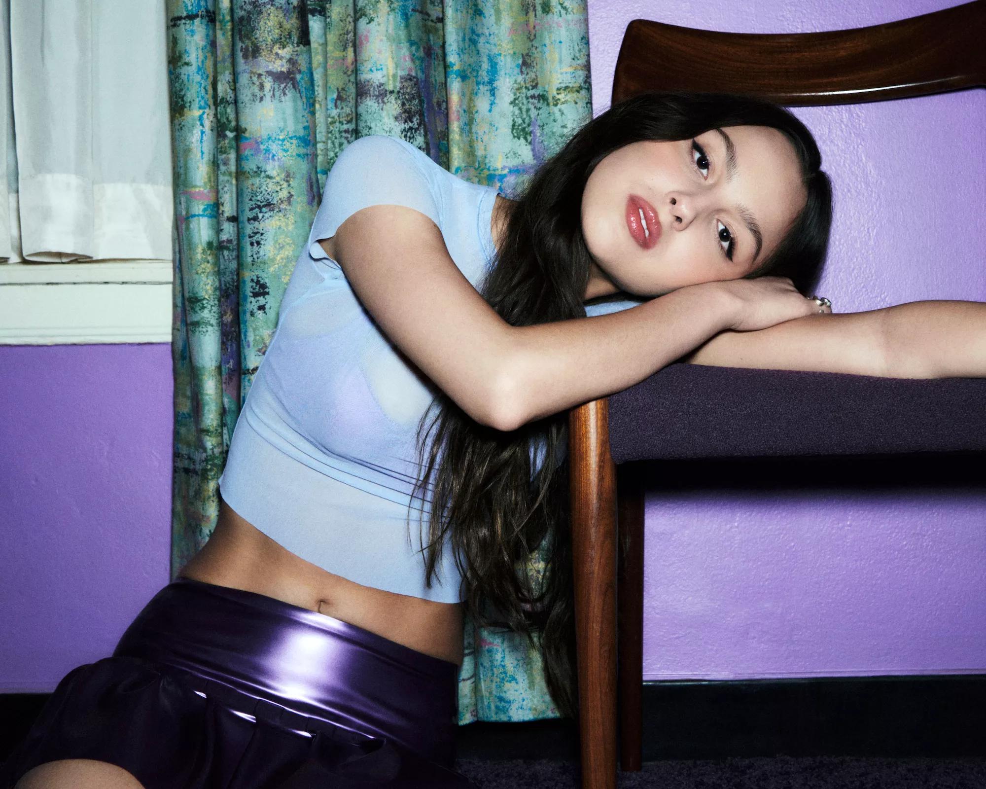 Olivia Rodrigo, laying her head on the seat of a chair