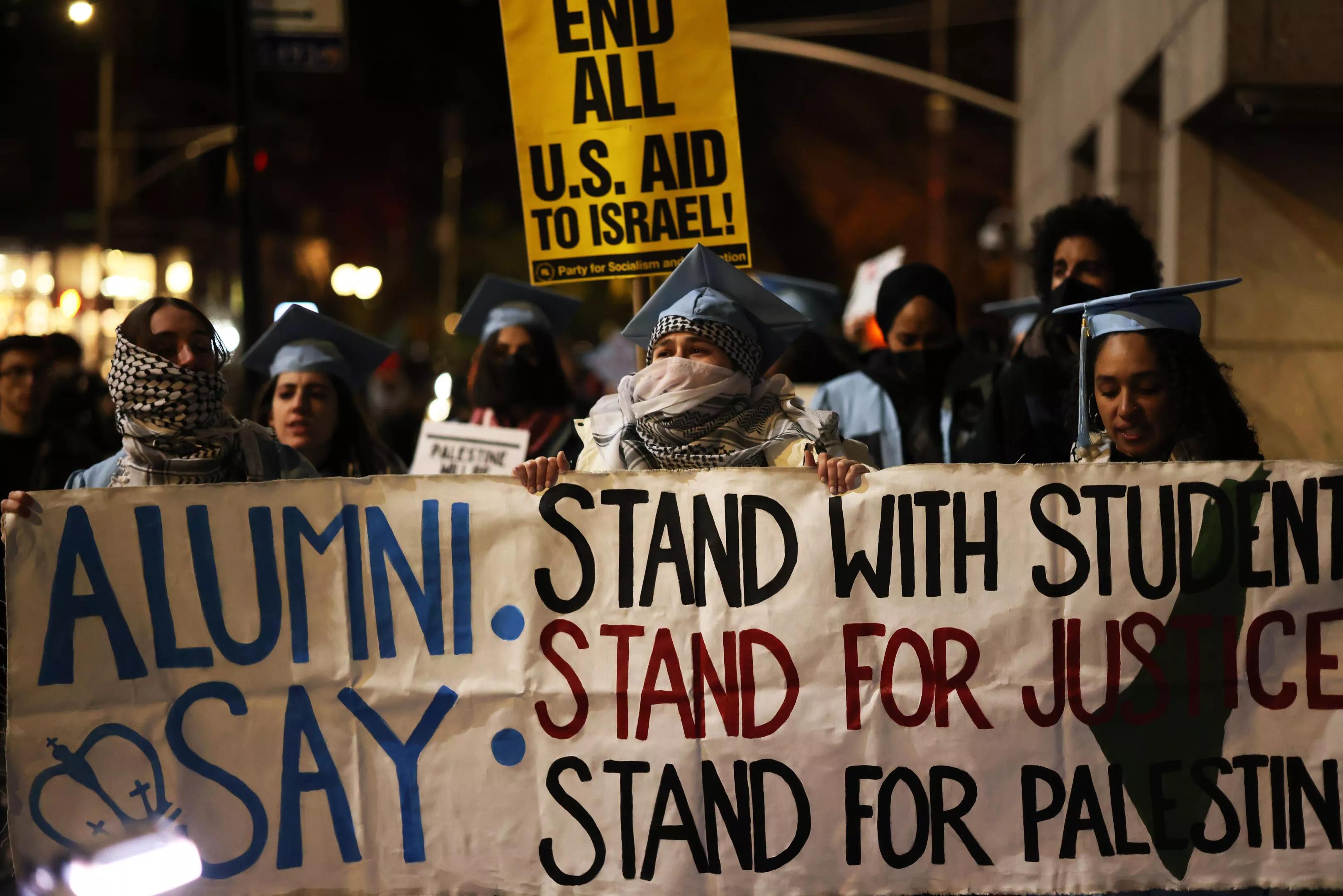 Protesters hold a large white sign, declaring, "Stand with students, stand for justice, stand for Palestine."