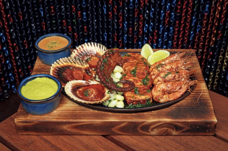 A dish of seafood and a green dip on a wooden table