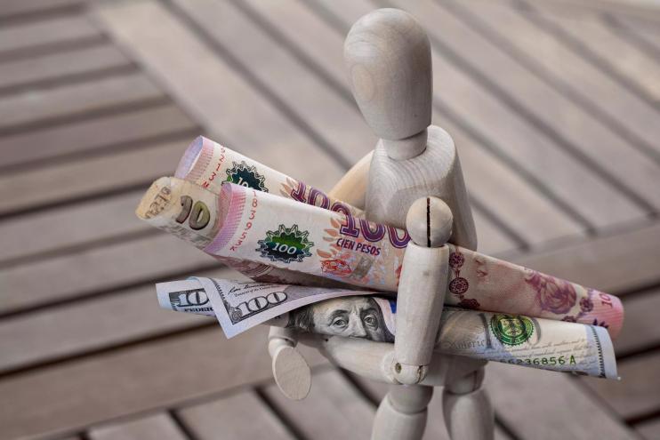 A stock photo of a faceless figurine carrying Argentinian pesos and U.S. dollars