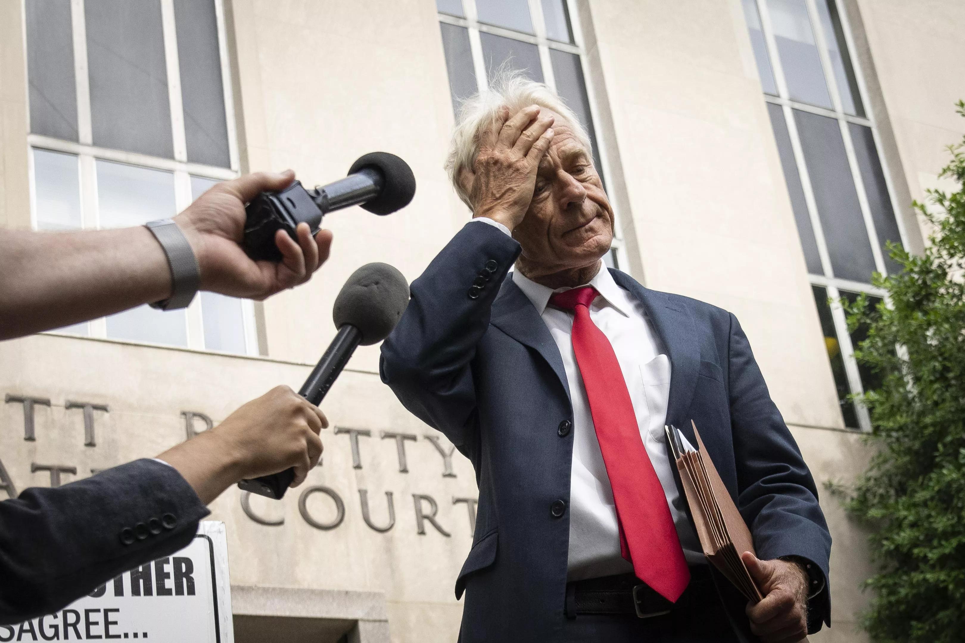 A Donald Trump adviser places a hand on his forehead as reporters stick out their microphones in front of a federal court