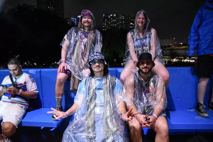 Four people in ponchos seated on blue plastic seats