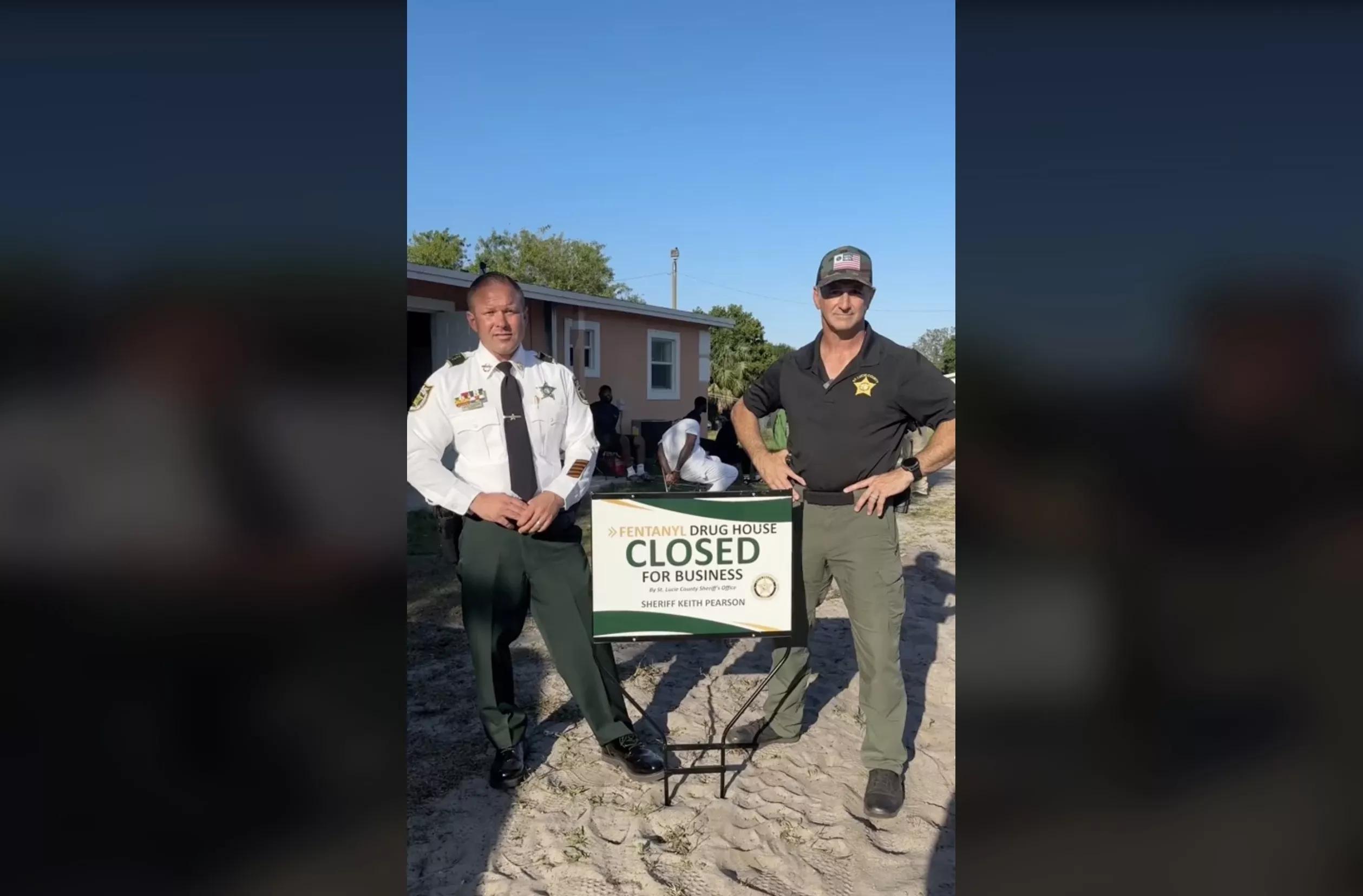 St. Lucie County Sheriff Pearson stands in front of a house in front of a self-promoting sign that says "Fentanyl Drug House CLOSED for Business"