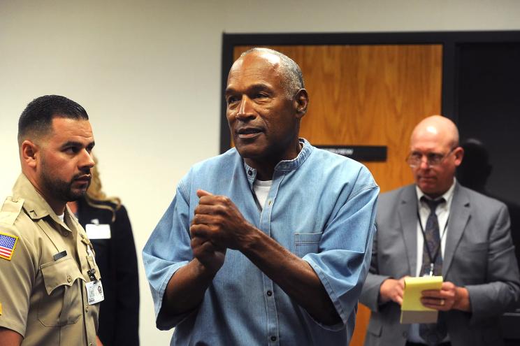 O.J. Simpson clasps his hands together in a courtroom while wearing an inmate's uniform