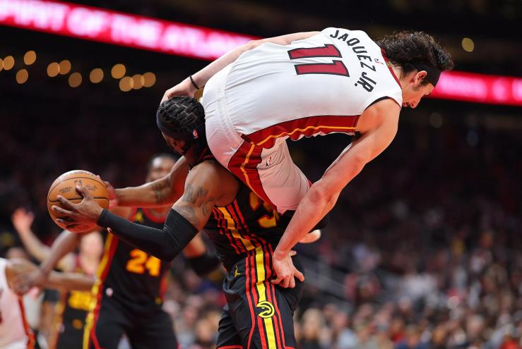 Jaime Jaquez of the Miami Heat is careening in the air during a game, with his derriere positioned on the neck of an Atlanta Hawks player