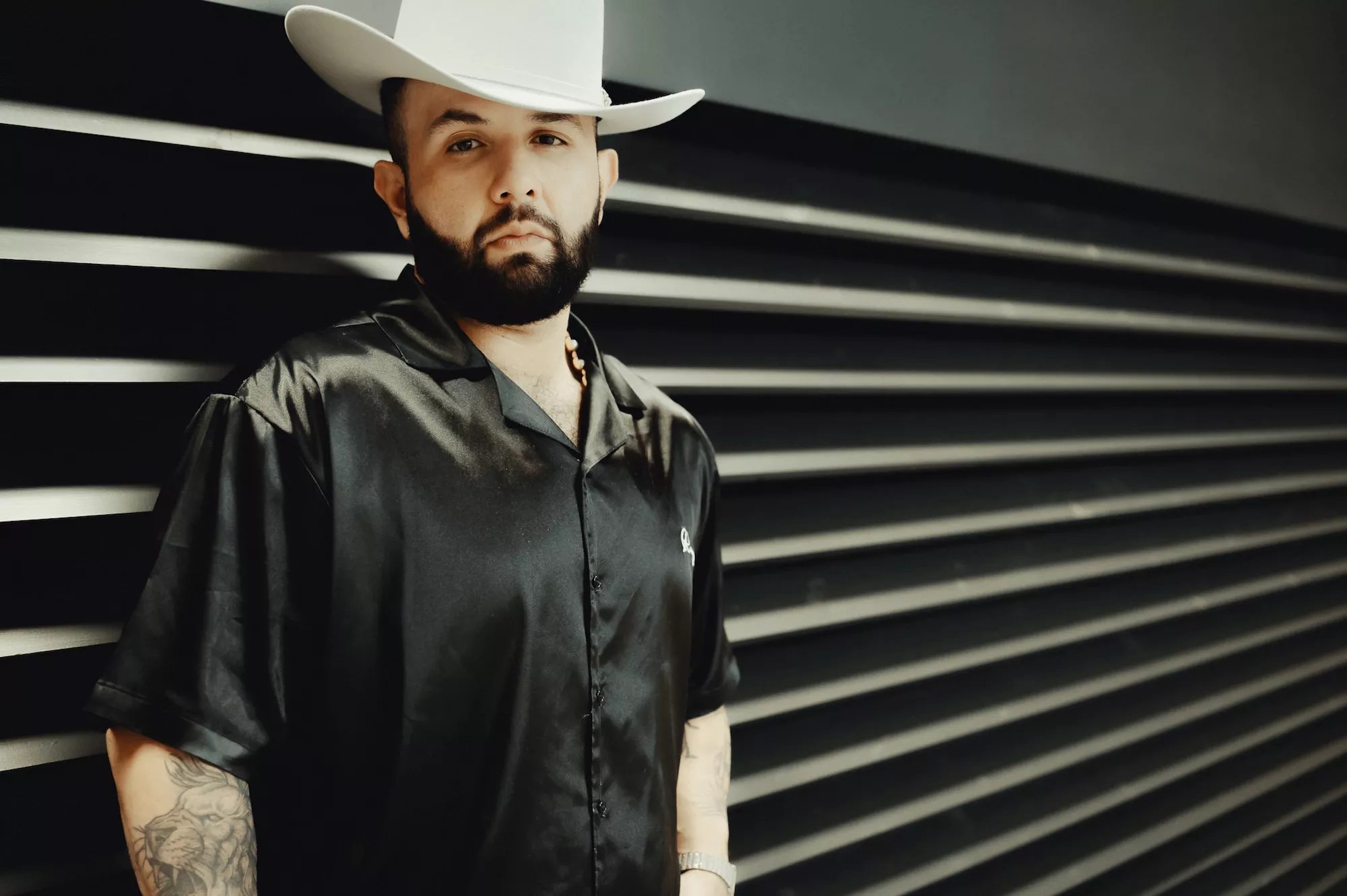 Carin León in a black shirt and white cowboy hat