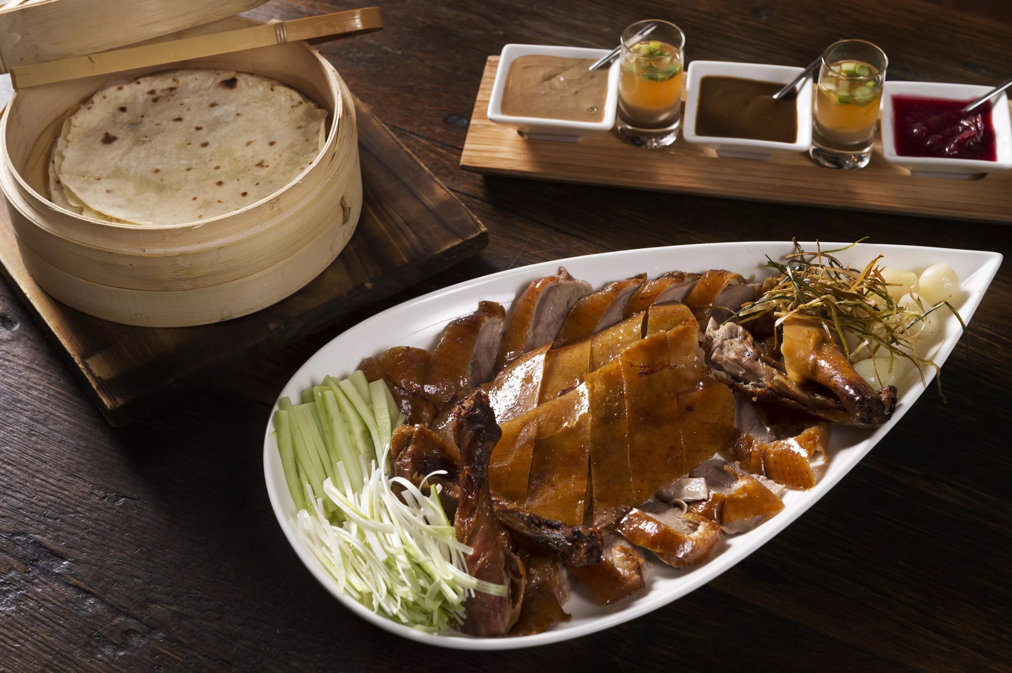 A duck dish on a white plate served with sauces on a wooden table