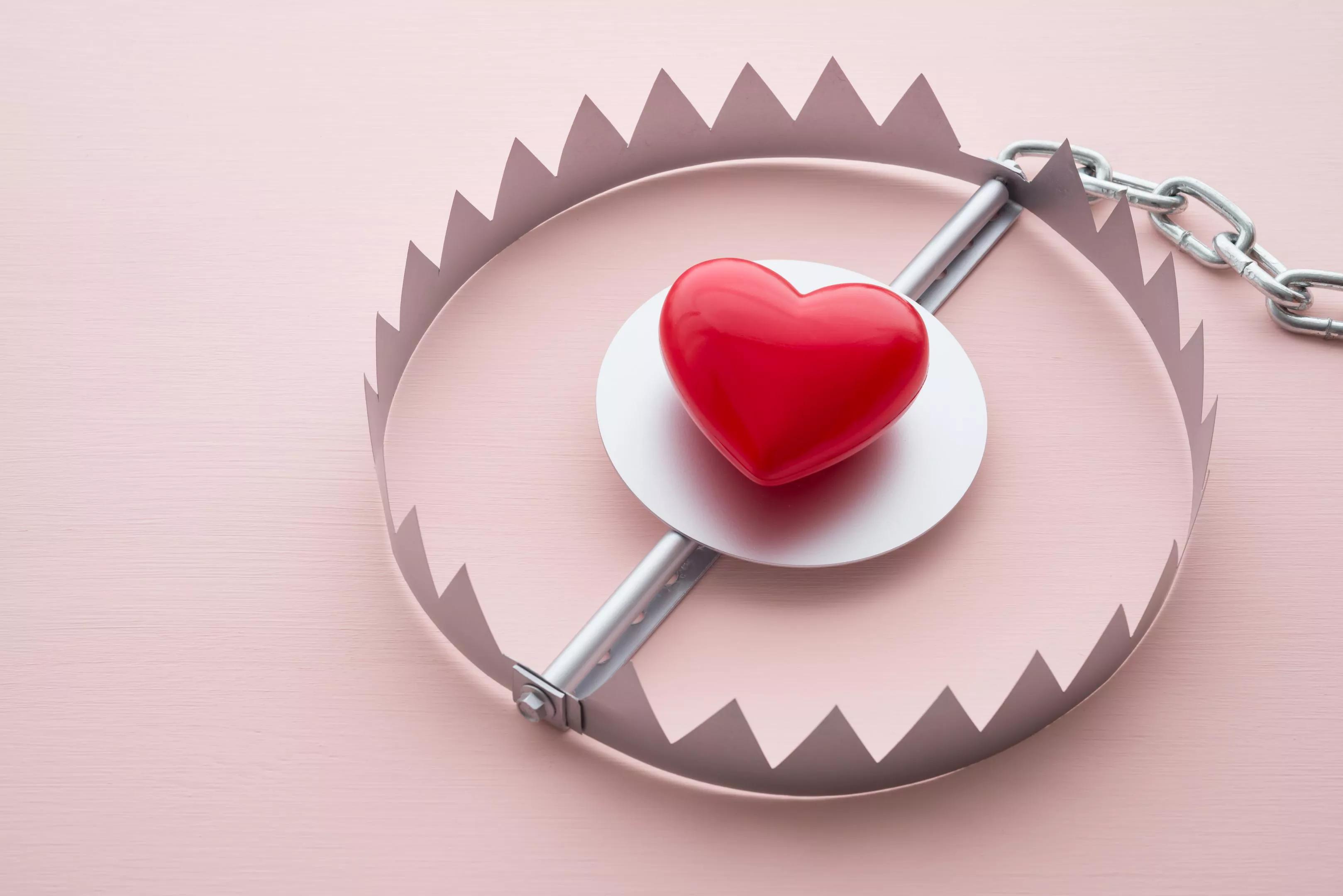 A bright red heart is surrounded by sharp, metal circular trap connected to a chain