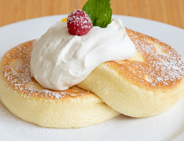 Pancake stack with cream and a strawberry on a white plate