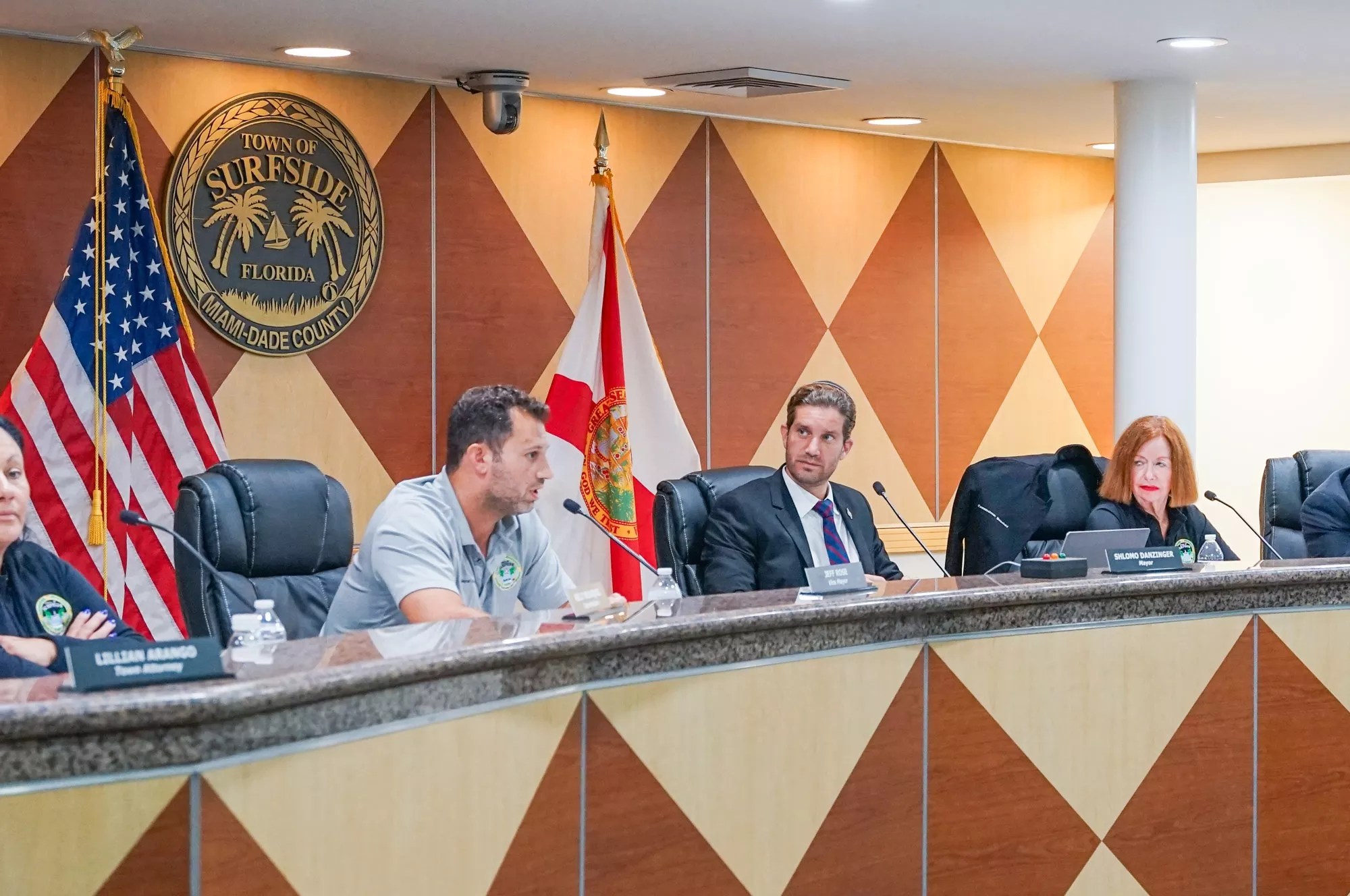Members of the Surfside town commission sit at the dais under a town crest