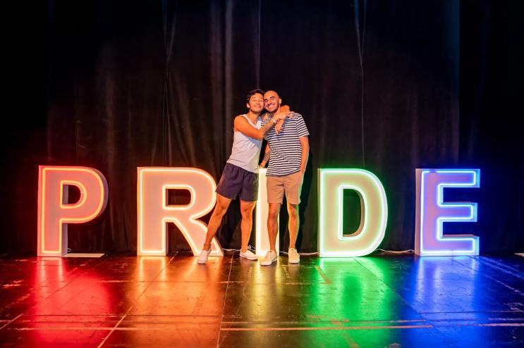 A gay couple in front of letters that spell out Pride