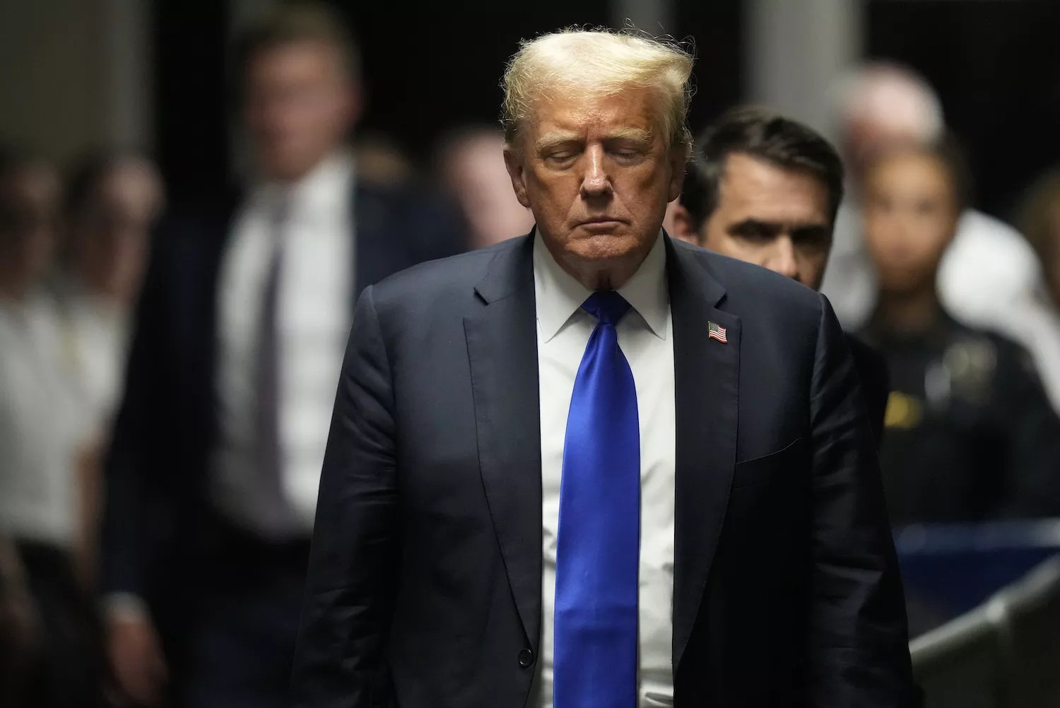 photo of Donald Trump wearing blue suit, white shirt, and blue(!) tie, walking, looking somber, with his eyes nearly closed