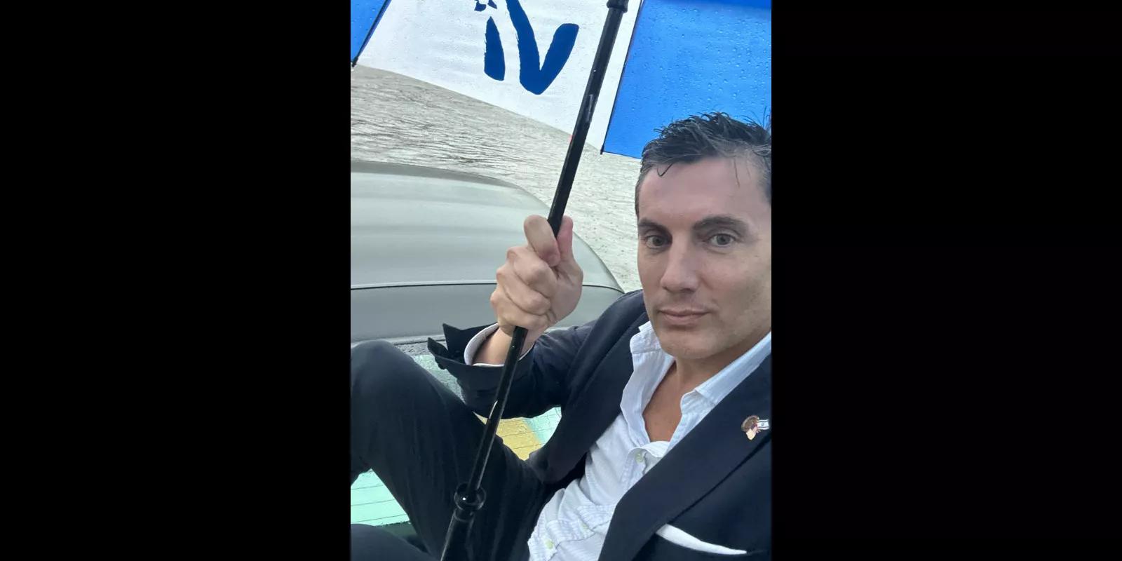 Fabián Basabe sitting on top of his car in a flood, with an umbrella