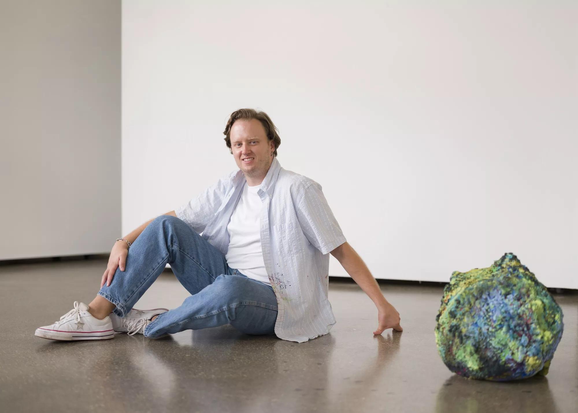 Portrait of artist Addison Wolff next to his artwork