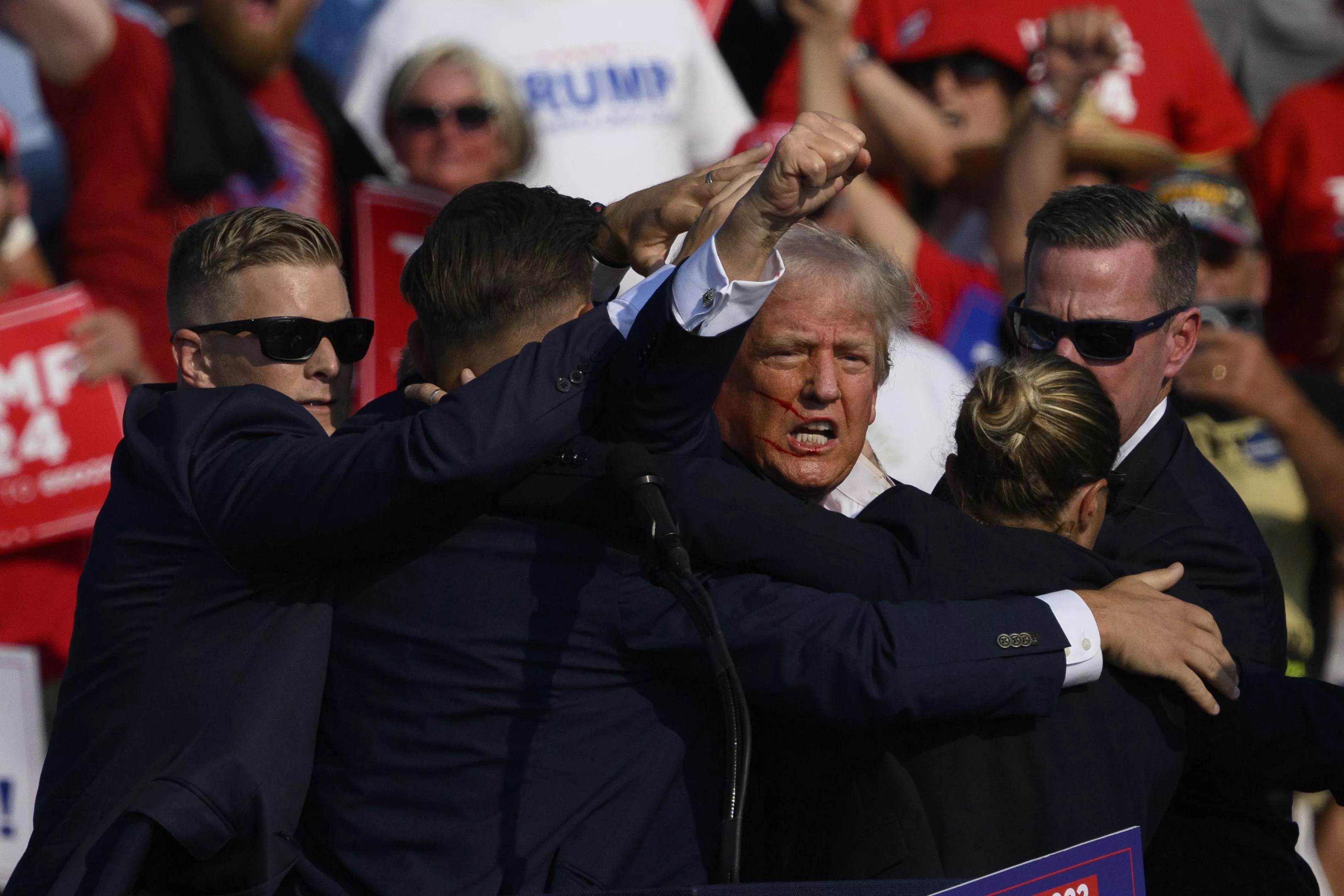 Former president Donald Trump pumps his fist, his face covered in blood, as Secret Service agents whisk him away