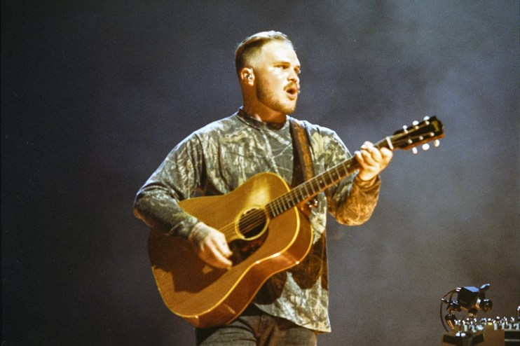 Zach Bryan with his guitar in hand performing on stage