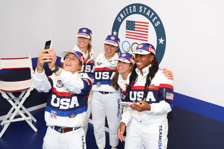 Five U.S. Olympians decked out in Olympic gear, smiling and huddled together in Paris
