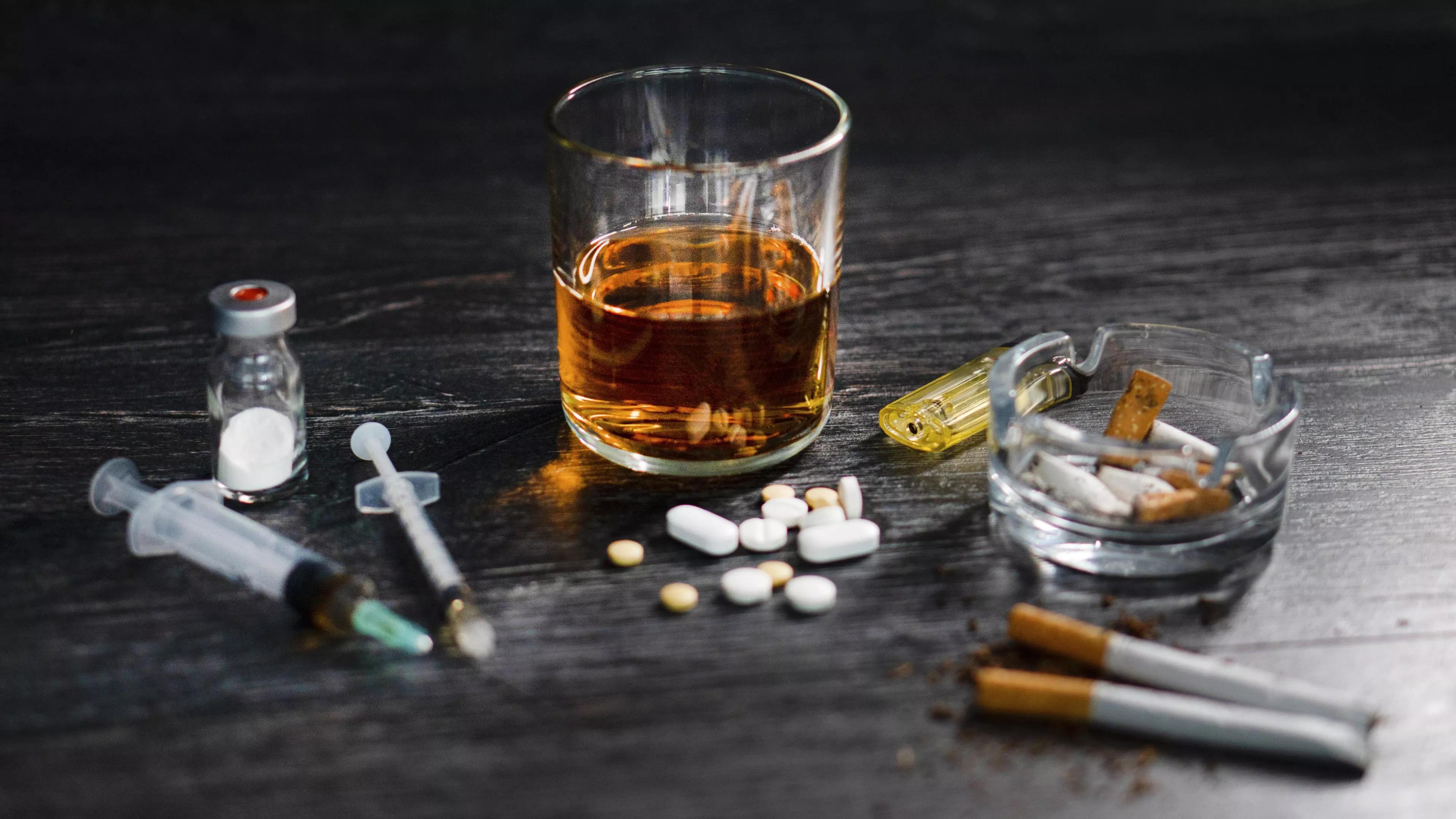 Pills, a glass of alcohol, and a needle splayed out on a table