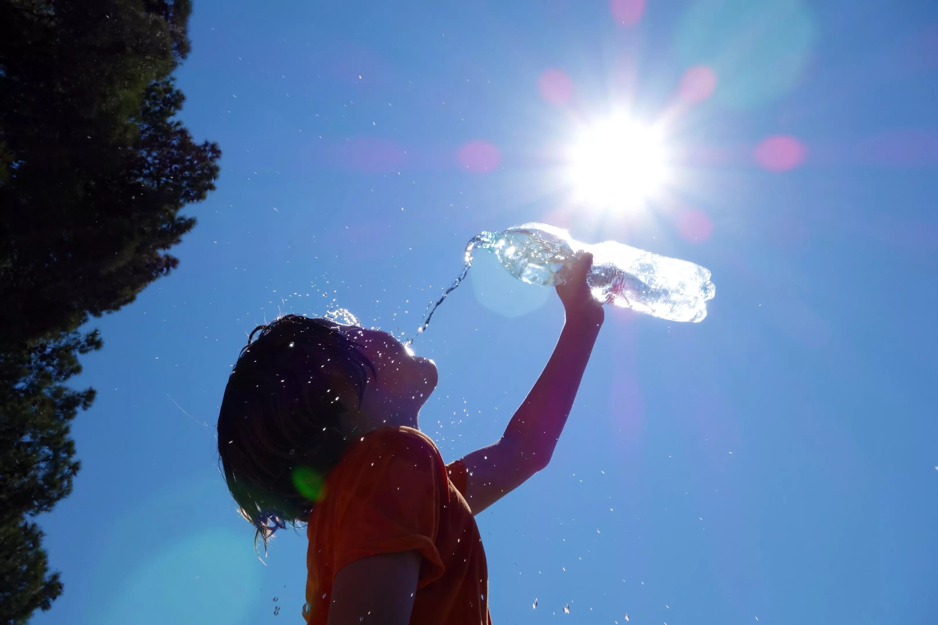 A child drinks from a water bottle with the sun beaming in the background