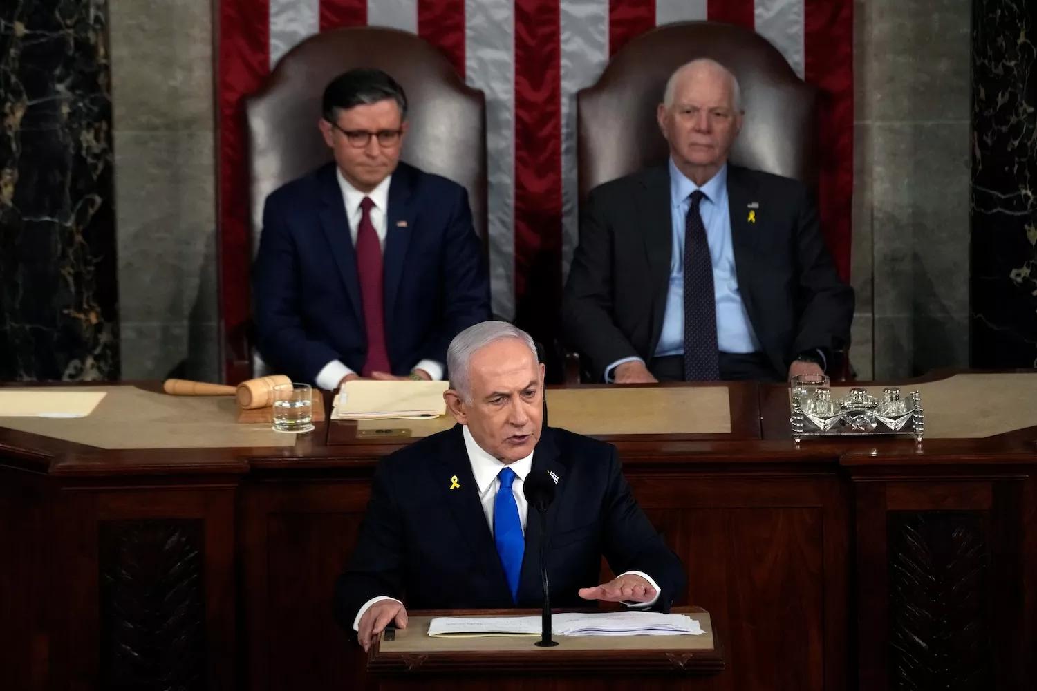 netanyahu at the dais with Speaker of the House Mike Johnson (R-LA) and U.S. Sen. Ben Cardin (D-MD) seated in the background, flanking him and slightly out of focus