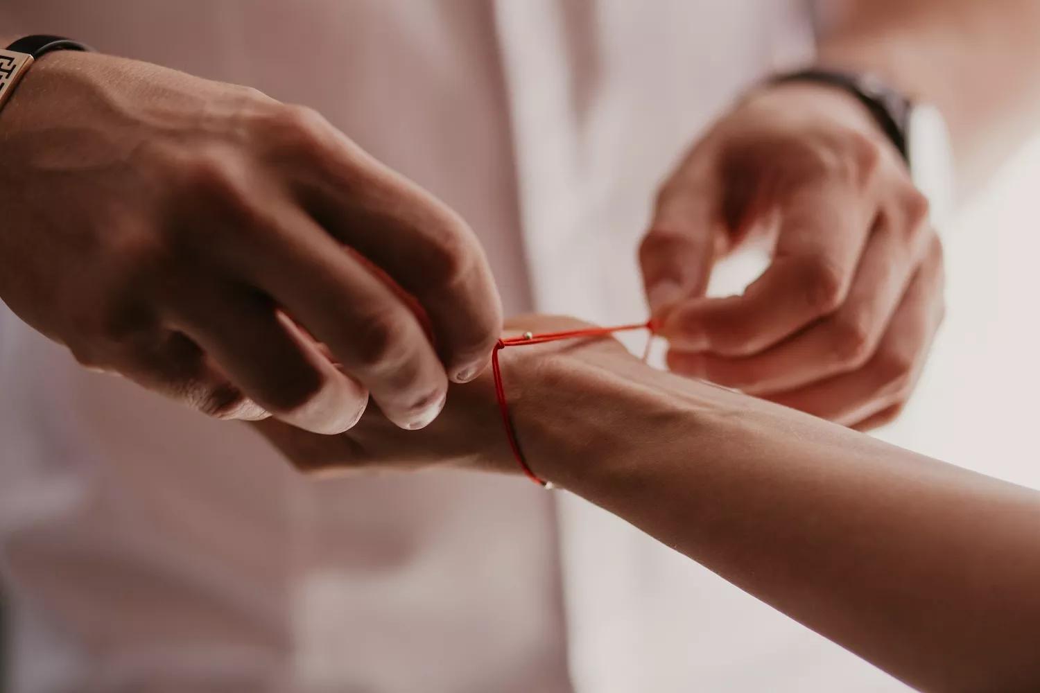 A man ties a red string bracelet on a woman's hand