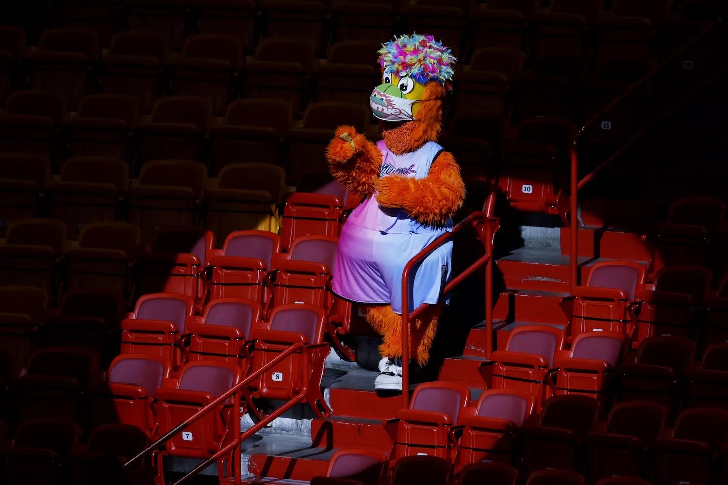 photo of Miami Heat mascot Burnie against a sea of empty arena seats, wearing a Pride-ish wig