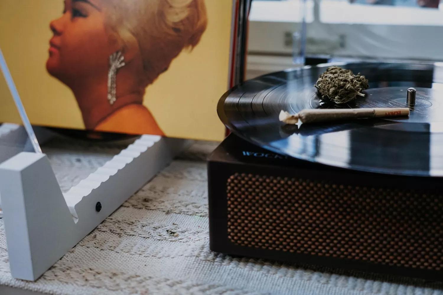 a joint and marijuana buds on a vinyl record on a turntable and part of the cover of Etta James's album "At Last" in the background