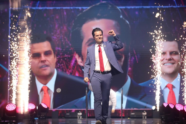 Matt Gaetz walks down the aisle of the stage with his fist in the air and sparklers in the background.