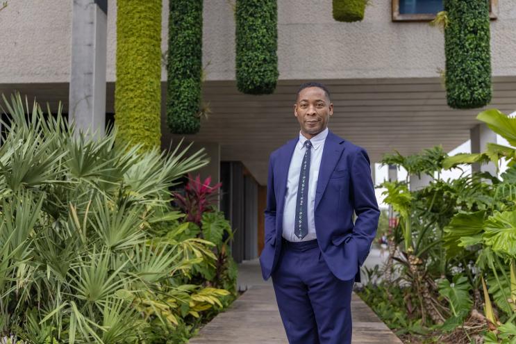 Portrait of Franklin Sirmans in a blue suit surrounded by greenery.