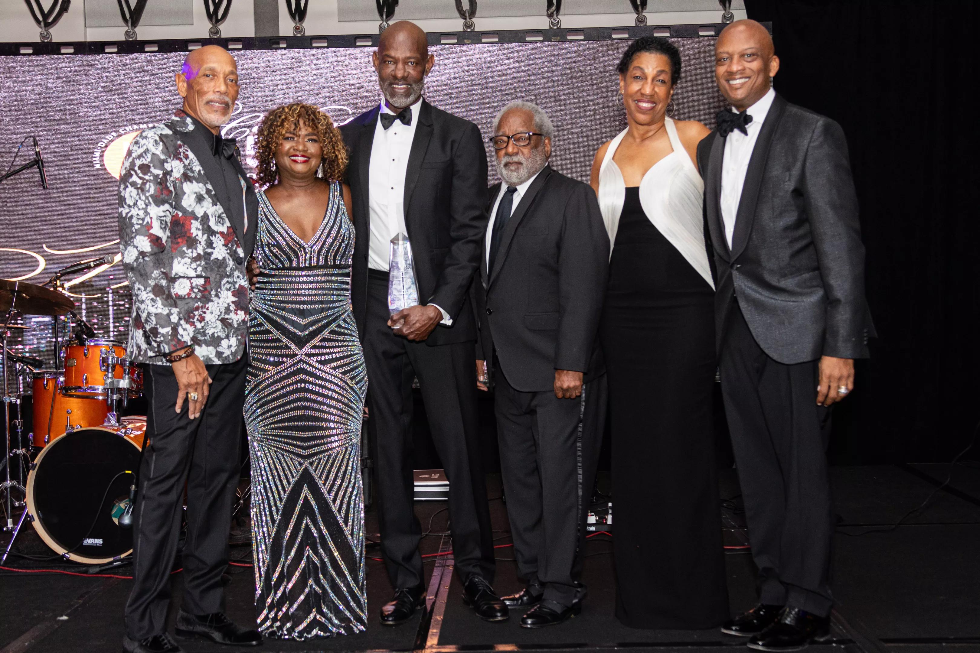 From left to right: Eric Knowles, Lynda Harris, Dr. Willie Logan, H.T. Smith, Teri Williams, and Commissioner Oliver G. Gilbert, III pose together on stage in formal attire during the Miami-Dade Chamber of Commerce’s gala.