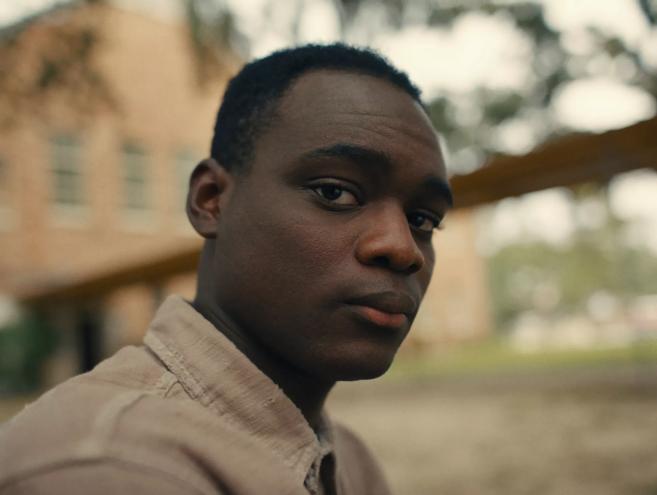 Still of the film Nickel Boys, with a close-up of Elwood (Ethan Herisse) staring into the camera.