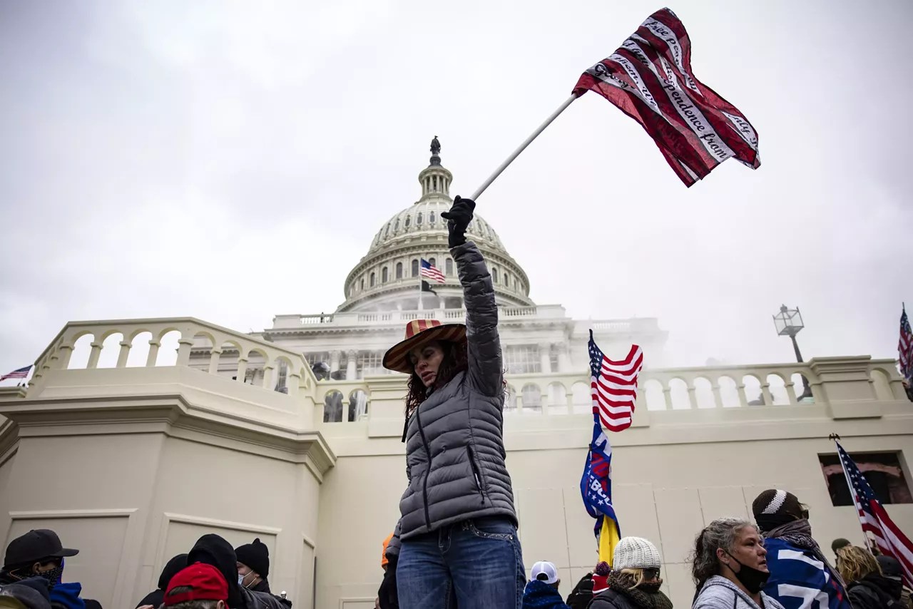 a woman in a red white and blue cowboy hat hoists a patriotic flag in front of the us capitol building