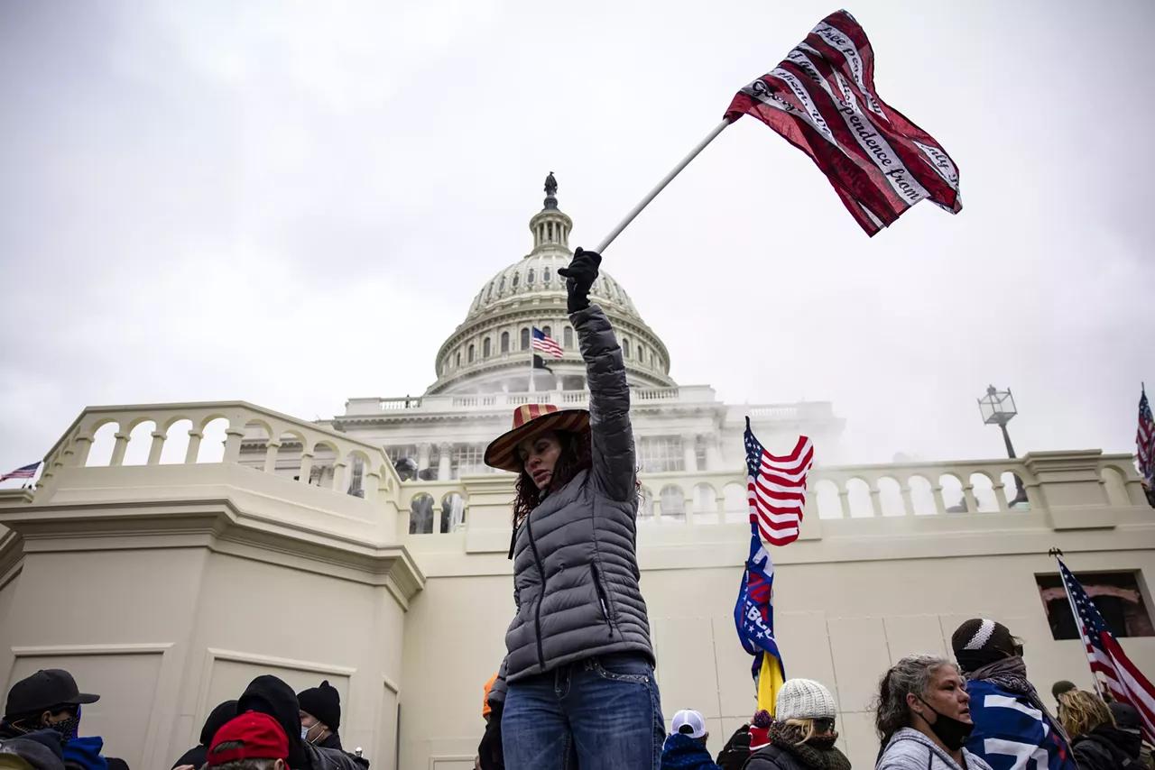 a woman in a red white and blue cowboy hat hoists a patriotic flag in front of the us capitol building