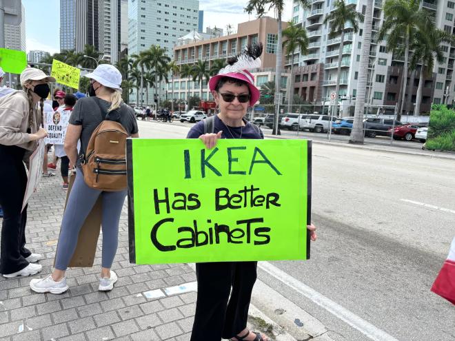 A protester at the Torch of Friendship holds a sign that reads, "IKEA has better cabinets."