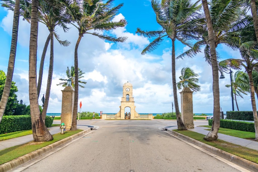 an image of the Worth Avenue clock tower with the Atlantic Ocean in the background and an avenue in the foreground, centering the distinctive clock tower
