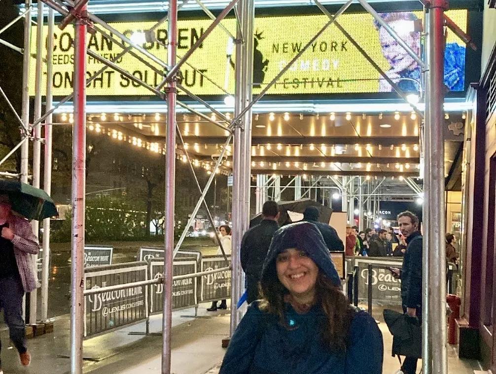 woman in a raincoat poses in front of the Beacon Theater marquee