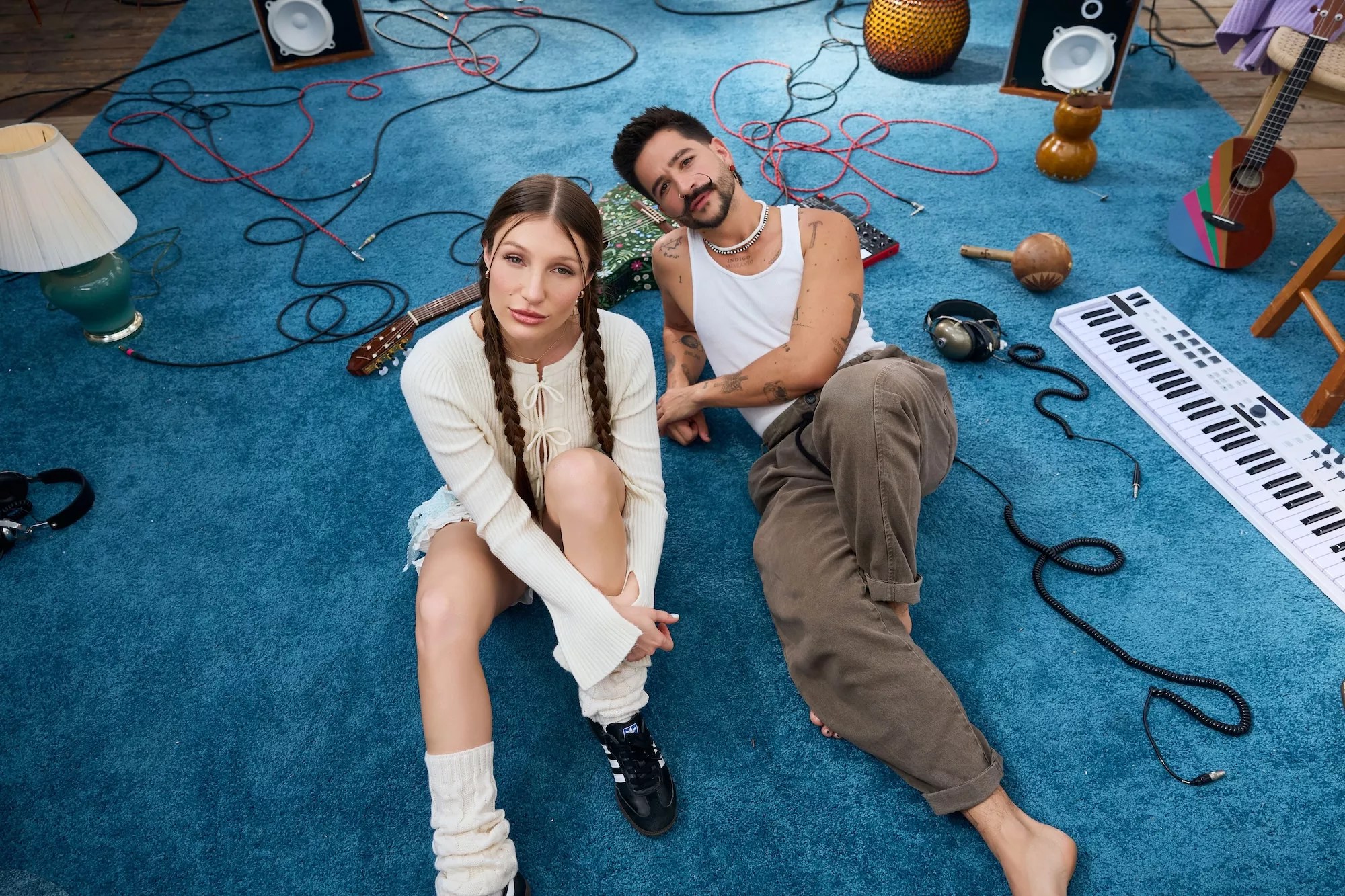 Yami Safdi and Camilo sitting on the floor cover in a blue carpet